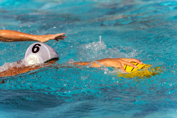 Number six in the white water polo uniform reaches for the ball while face is submerged under water.