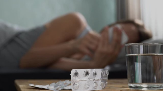 A lonely sick girl looks at her cell phone, counting the minutes until the pain subsides. A woman lies on the bed and hurts. There are Antidepressants on the bedside tables. Virus Allergy Infection