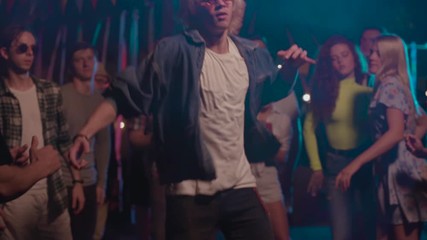 Cool party dancer blonde boy dancing like robot with robotic moves in front of happy friends watching enjoying music in neon nightclub.