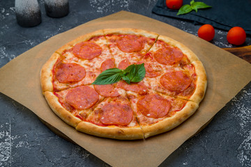 Pepperoni pizza with basil on board on dark grey concrete table