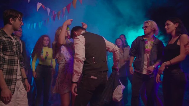 Handsome positive businessman dancing sexy lambada dance with attractive blonde girl in the crowd. Excited young people hanging out in the nightclub disco celebration.