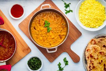 Indian Food: Curry Pot Full of Pea and Potato with Rice Bowl, Dal Pot, Naan Bread and Spices.