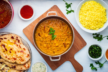 Indian Food: Curry Pot Full of Pea and Potato with Rice Bowl, Dal Pot, Naan Bread and Spices.