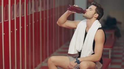 Tired sportsman drinking water in dressing room.