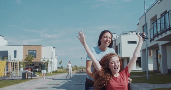 Pretty smiling young woman riding her friend in wheelchair for fun. Lovely ginger curly girl raising hands enjoying freedom motion fresh air.
