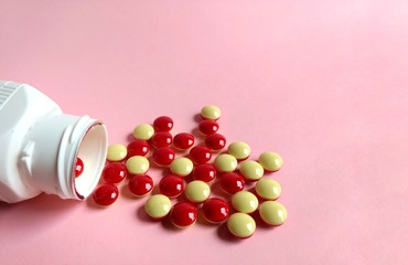 Scattered red and yellow pills with pill bottle on pink background. medical concept