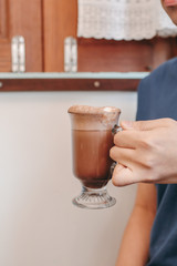 A glass with coffee drink with cream white topping in the hands of young man in black t-shirt, copy space. Wide panoramic image, Texture white background.