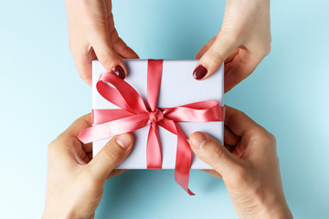 Male hands passes gift box to female hands, blue background