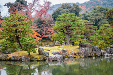 Japanese garden island with old gray stones and perfectly pruned pine trees that reflect in the smooth water of a pond