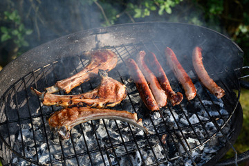 Quatre saucisses et trois de cotes d'agneaux sur un barbecue dans un jardin vues de près