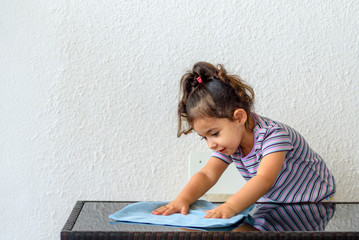 Fototapeta premium Cute brunette child helping her mom washing modern design garden furniture, glass table on home terrace. Little girl make cleaning with water and blue towel.