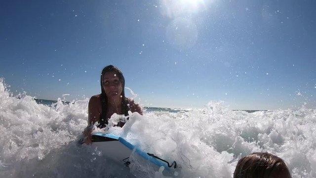 3 young women having fun boogie boarding at the beach as they ride a wave into shore.