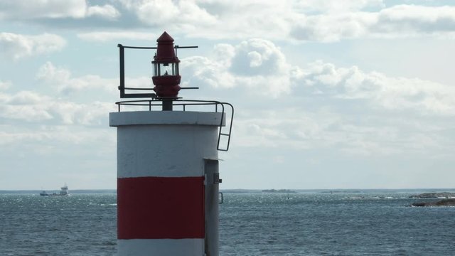 Lighthouse close up, calm waters, cargo ship passing in the distance. Baltic sea, Oxelosund, Sweden.