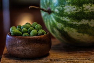 Still Life of a Large Watermelon on a Wooden Board next to a small wooden bowl of Mexican Sour Gherkins, selective focus on foreground
