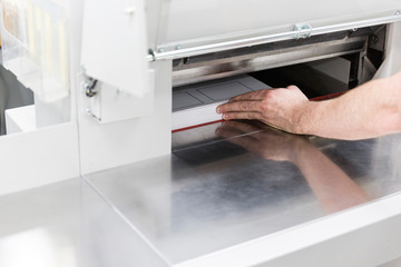 Professional printer realigning paper in guillotine.