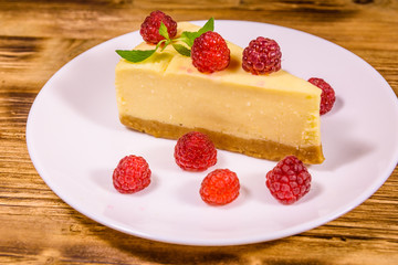 White plate with cheesecake New York, leaf of mint and raspberries on wooden table