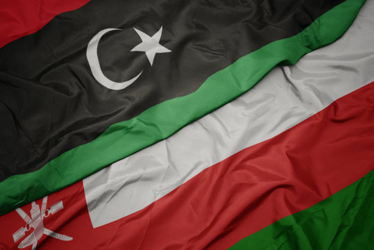 waving colorful flag of oman and national flag of libya.