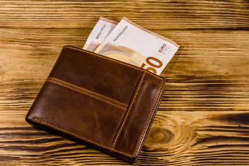 Brown leather wallet with fifty euro banknotes on the wooden background