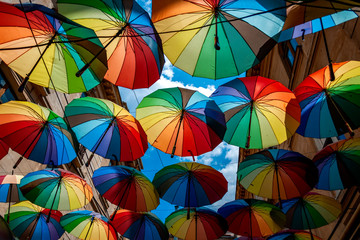 Fototapeta na wymiar Protection against rain, multicolored parasol and shelter from the sun conceptual idea with lots of colourful flying umbrellas with each umbrella painted in vivid multicoloured rainbow colour