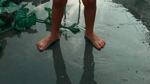 lonely child insolation outcast depression child abuse young boy shadow silhouette playing sliding his barefoot side to side in a water puddle sky and clouds reflection childhood fun and games