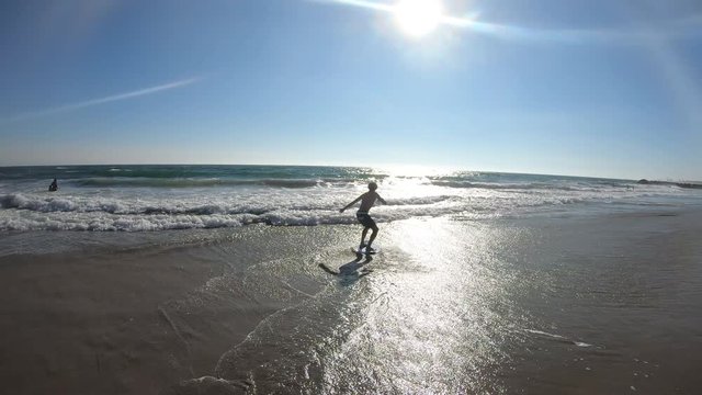 Young man running on beach and jumping on skim board riding it into the ocean at the beach.