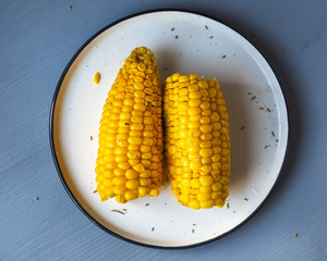 Freshly cooked ripe corn from two halves on a round plate, top view