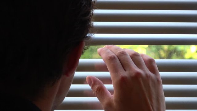 Curious man looking through Venetian window. Hand revealing white Venetian blinds