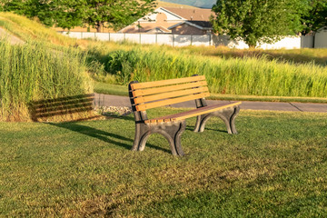 Empty outdoor park bench casting shadow on the grassy terrain on a sunny day