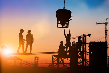 Silhouette Two engineers consult and inspect high-rise construction work over blurred industry...