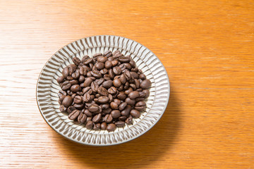 Coffee beans on a plate placed on a wooden table.