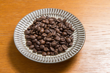 Coffee beans on a plate placed on a wooden table.