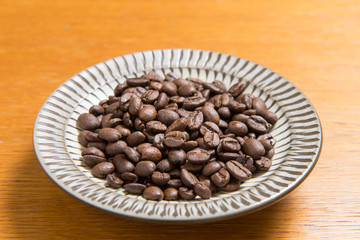 Coffee beans on a plate placed on a wooden table.