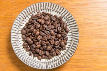 Coffee beans on a plate placed on a wooden table.