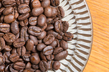 Coffee beans on a plate placed on a wooden table.