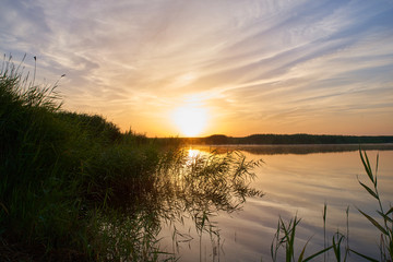 Spectacular morning landscape of bushy river banks and smooth river waters against warm colors of early morning sun. Magnificent sunrise over distant forests and the river in Russian countryside. 