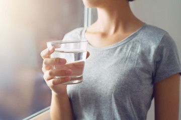 young woman standing and holding glass water near window. concept healthy