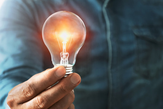 businessman hand holding lightbulb with sunshine. concept saving energy power
