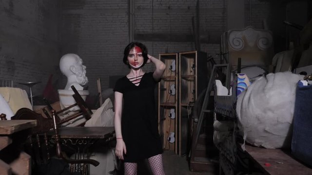 upset girl with artistic makeup raises hands performing pantomime in old studio with stacked objects slow motion