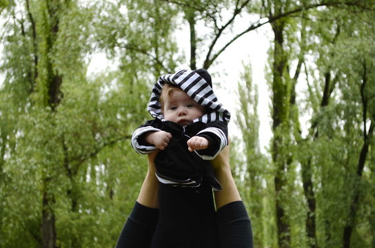 European baby 4 months in a striped hood and a black jacket in hands his dad in the spring forest