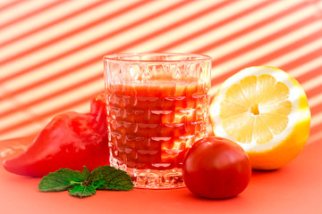 vegetable juice (smoothie) among vegetables (pepper, tomato, lemon, mint) on a red background with stripes of light