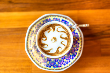 A cup of hot milk  in an antique Thai traditional benjarong style containers, on wood  table, Sensitive focus.