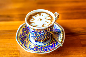 A cup of hot milk  in an antique Thai traditional benjarong style containers, on wood  table, Sensitive focus.