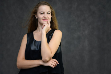 Studio photo portrait of a pretty student girl, brunette young woman with long beautiful hair in a black T-shirt on a gray background. Smiling, talking, showing emotions