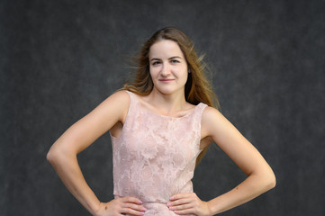 Studio portrait on the waist of a pretty student girl, a young brunette woman with long beautiful hair in a pink dress on a gray background. Smiling, talking, showing emotions