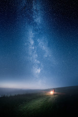 A man with lantern walking on a field at night with epic milky way on the sky