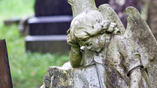 Angel girl stone grave headstone in rainy cemetery. Sad, mourning, sorrow remembrance figure.