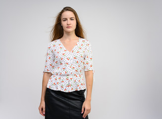 Studio photo portrait of a pretty student girl, young brunette woman with long beautiful hair in a light blouse and a black skirt on a white background. Smiling, talking, showing emotions