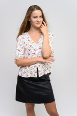 Studio photo portrait of a pretty student girl, young brunette woman with long beautiful hair in a light blouse and a black skirt on a white background. Smiling, talking, showing emotions