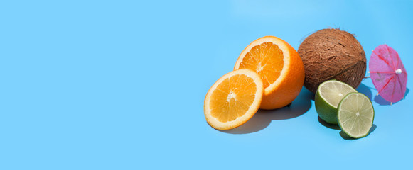Fresh juicy orange, coconut and green lime with a cocktail umbrella isolated on blue background. Concept of Healthy eating and dieting. Travel and holiday concept. Copy space. Free space for your text