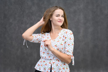 Studio portrait of a pretty student girl, young brunette woman with long beautiful hair in a light blouse on a gray background, waist-high. Smiling, talking, showing emotions